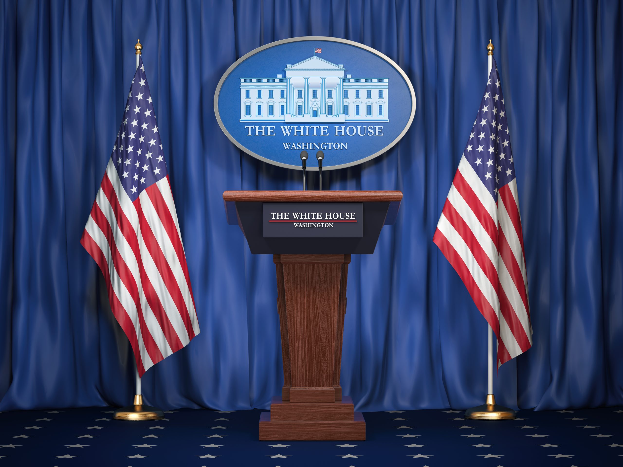 A podium with 2 American flags standing on either side, and a large plaque with a picture of the white house behind it, on a long blue curtain.