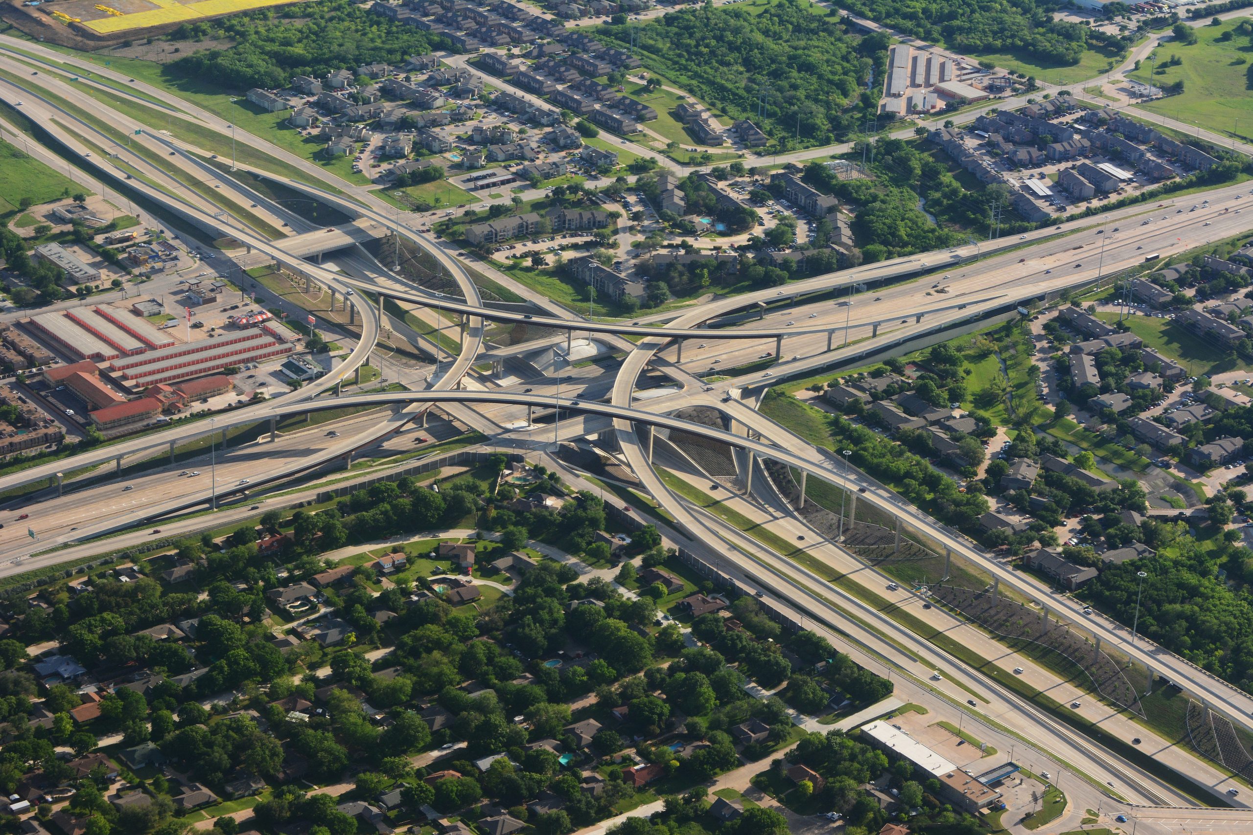 intersecting highways coming from four different directions, creating a cross, surrounded by greenery, buildings, and cars.