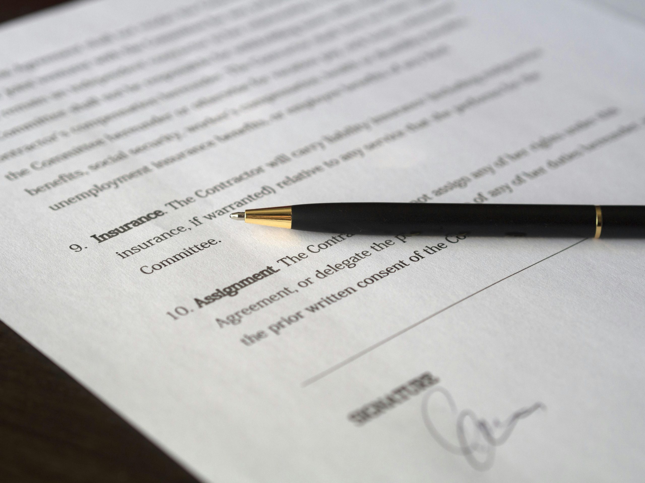 typed text of a contract agreement in black ink, printed on white paper, with a black pen on top of the paper